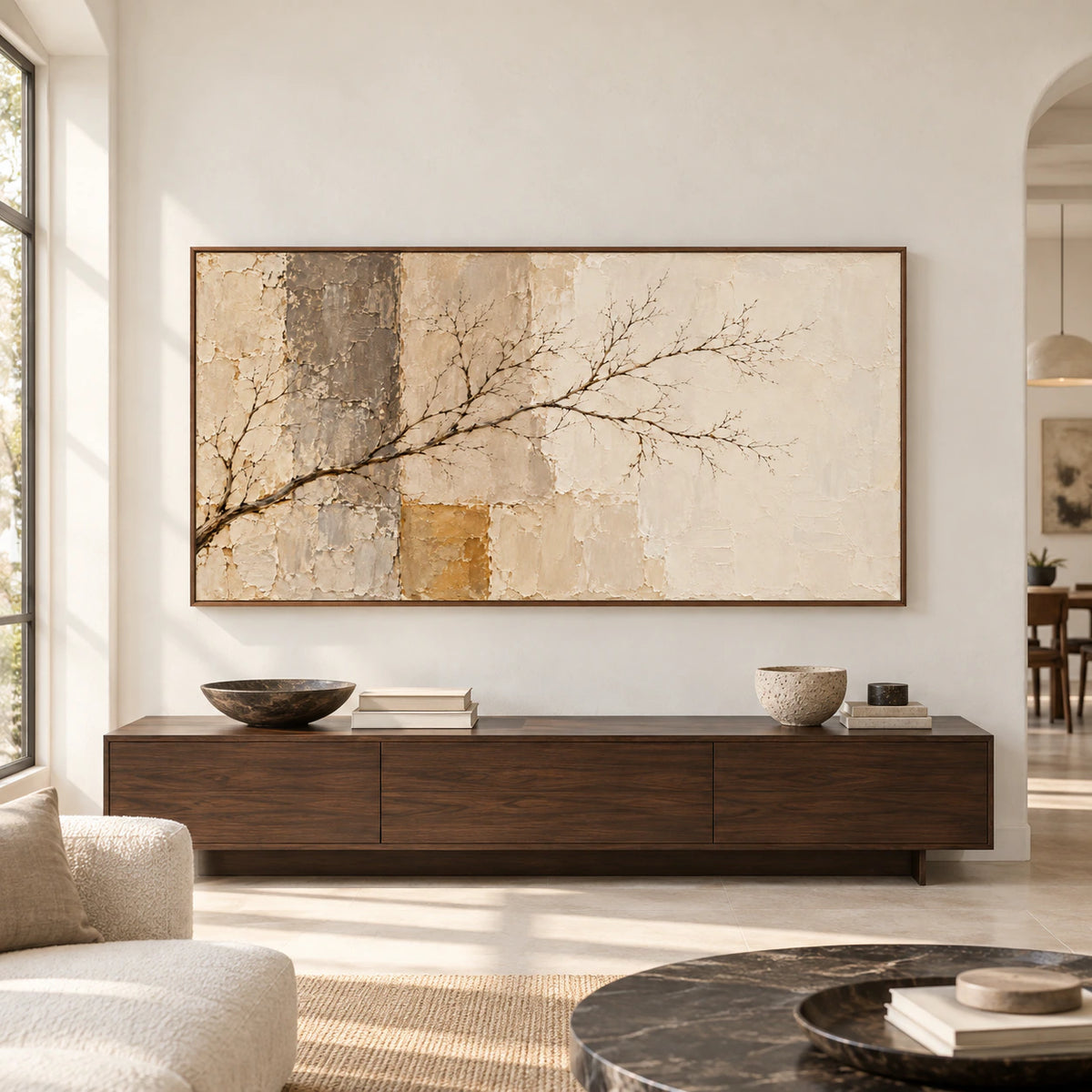 Large horizontal artwork with a dark branching limb across weathered cream, sand and ochre patches, centered above a long console in a spacious gallery-like room.