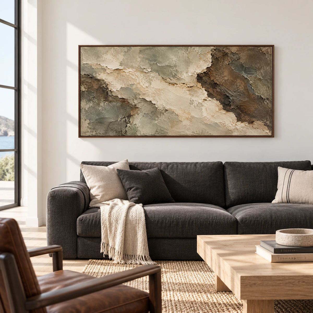 Left-oblique view of a wide textured abstract painting above a charcoal sofa in a bright living room with pale walls.
