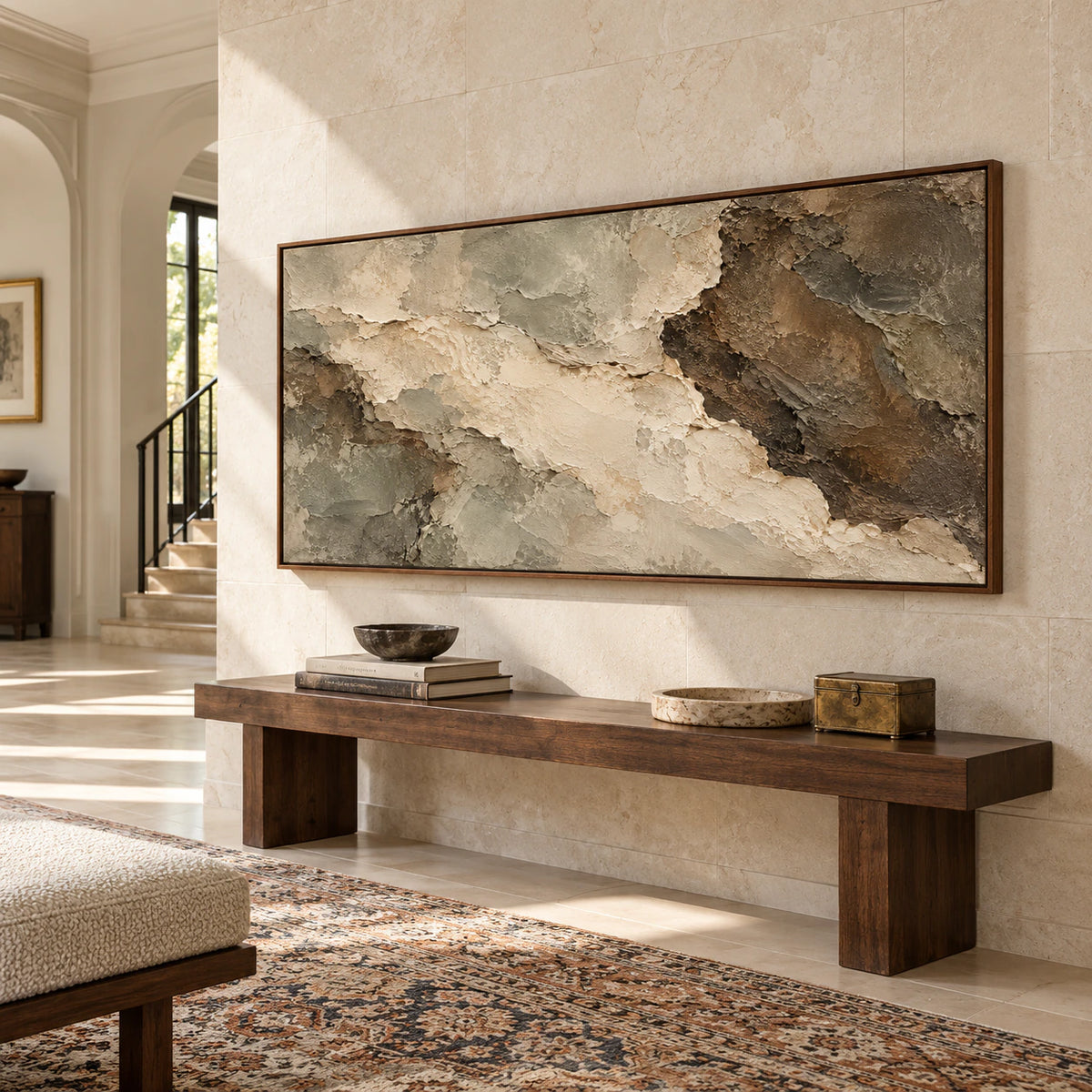 Low, left-oblique view of a large textured abstract painting above a substantial console against a tall pale stone wall in a bright foyer.