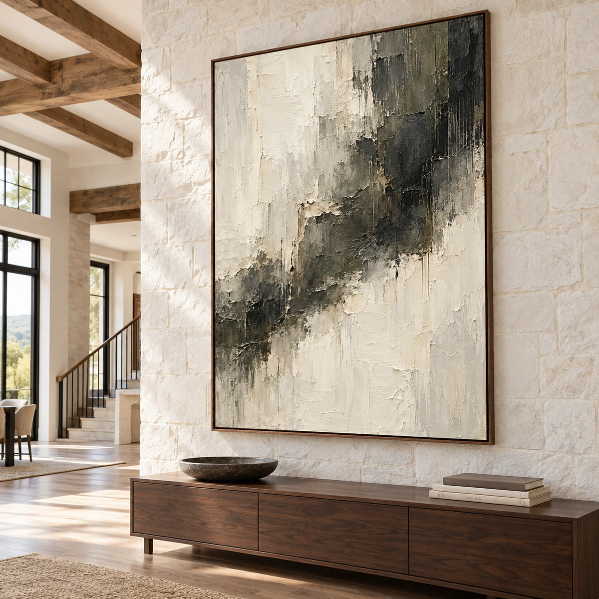 Large ivory and charcoal abstract painting on a tall pale stone wall in a bright foyer with wood flooring and a dark wood console, viewed from a low left angle.