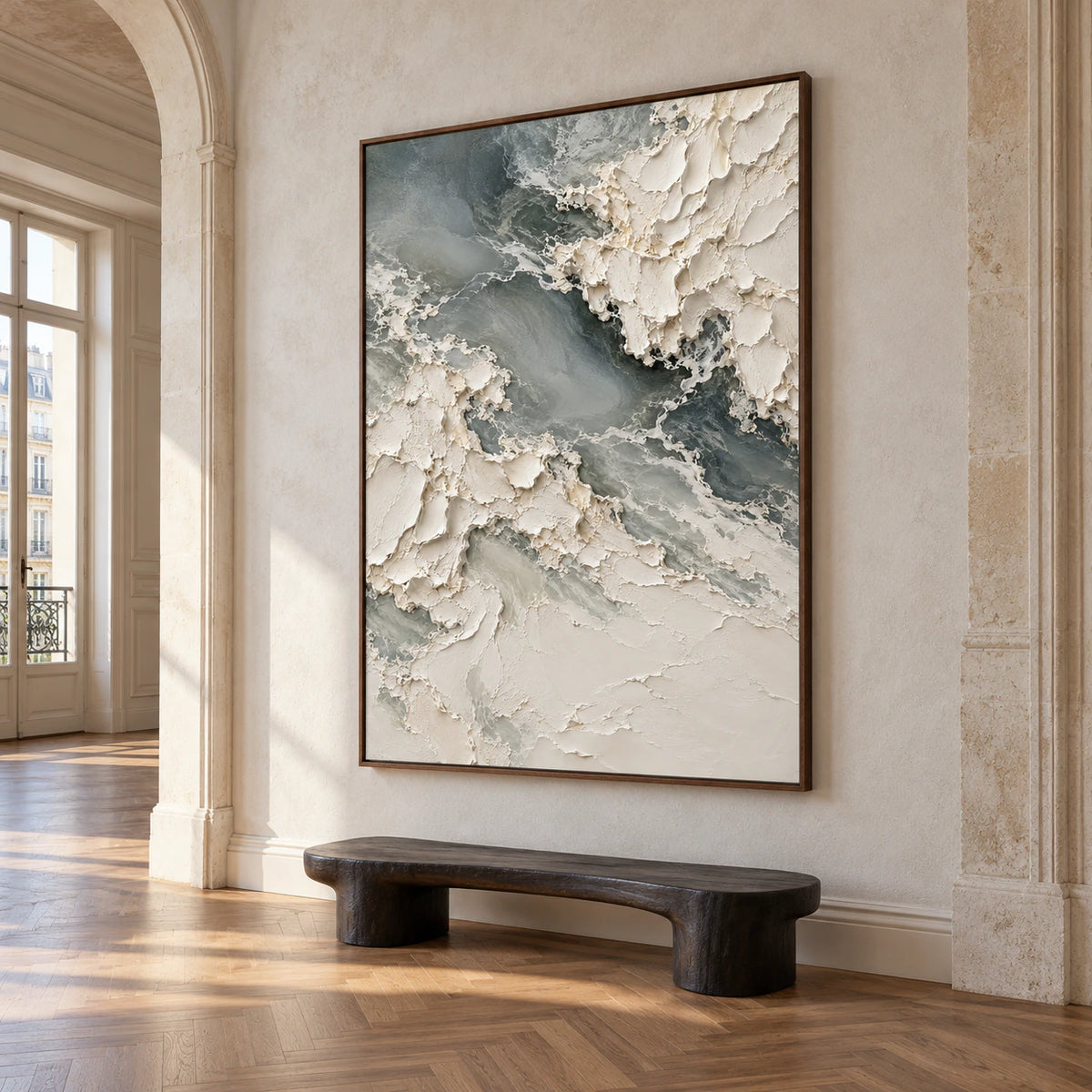 Chalkwater-Fold on a pale stone foyer wall beside a dark sculptural bench, viewed from a low left angle beneath a high ceiling.