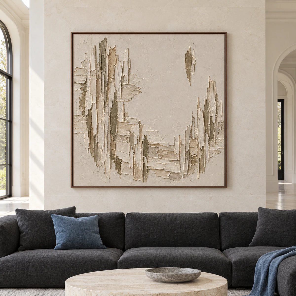 Straight-on view of a large square textured painting on a pale limestone wall in a spacious living room with dark charcoal seating and natural daylight.