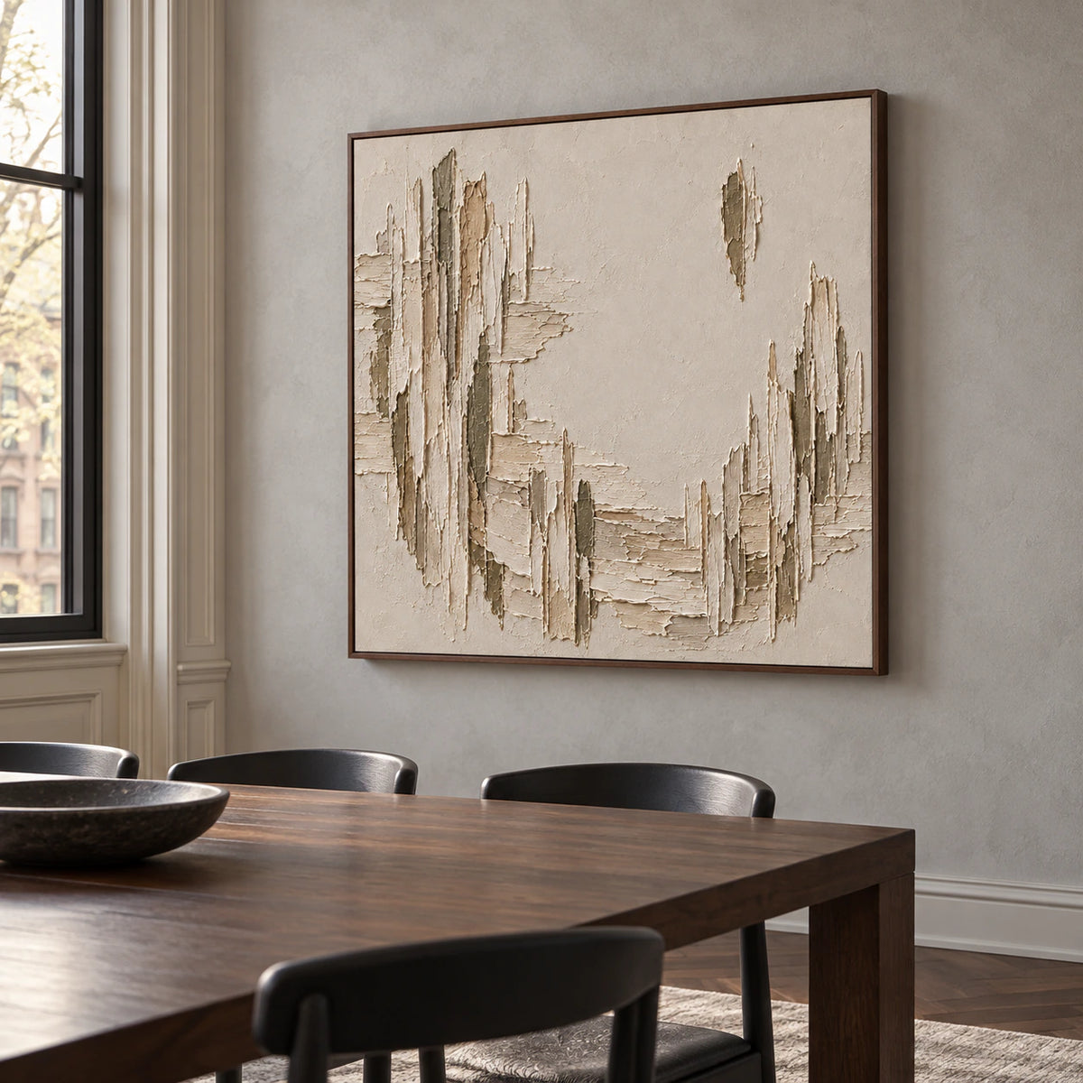 Right-oblique view of a square textured painting on a cool-gray plaster wall above a dark walnut dining table with simple black chairs.