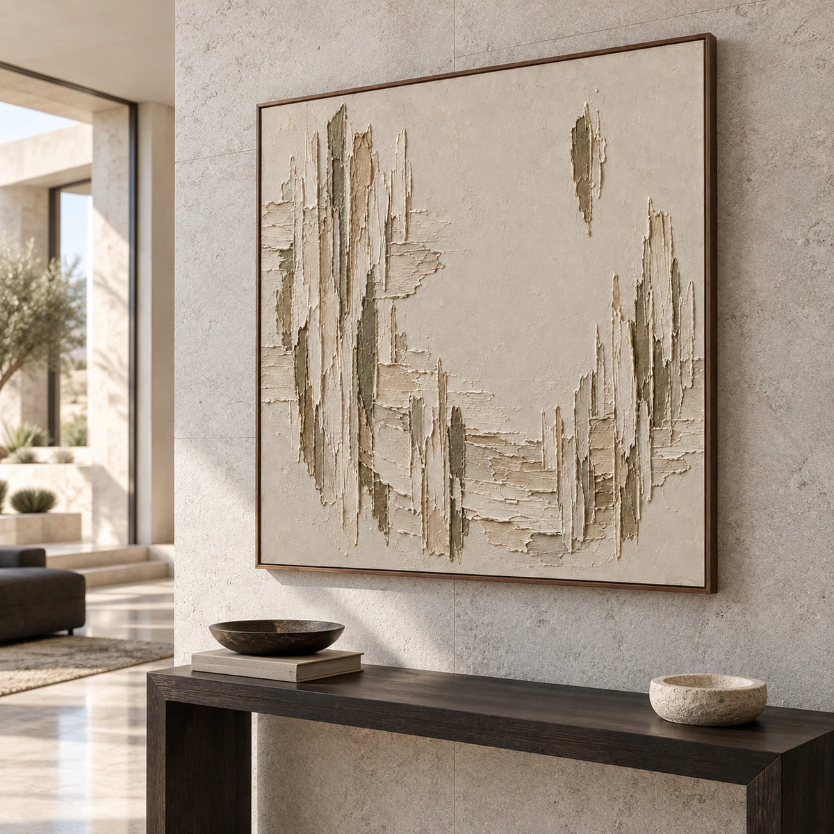 Slightly elevated left-oblique view of a square textured painting on a pale gray stone wall above a narrow dark console in a spacious foyer.