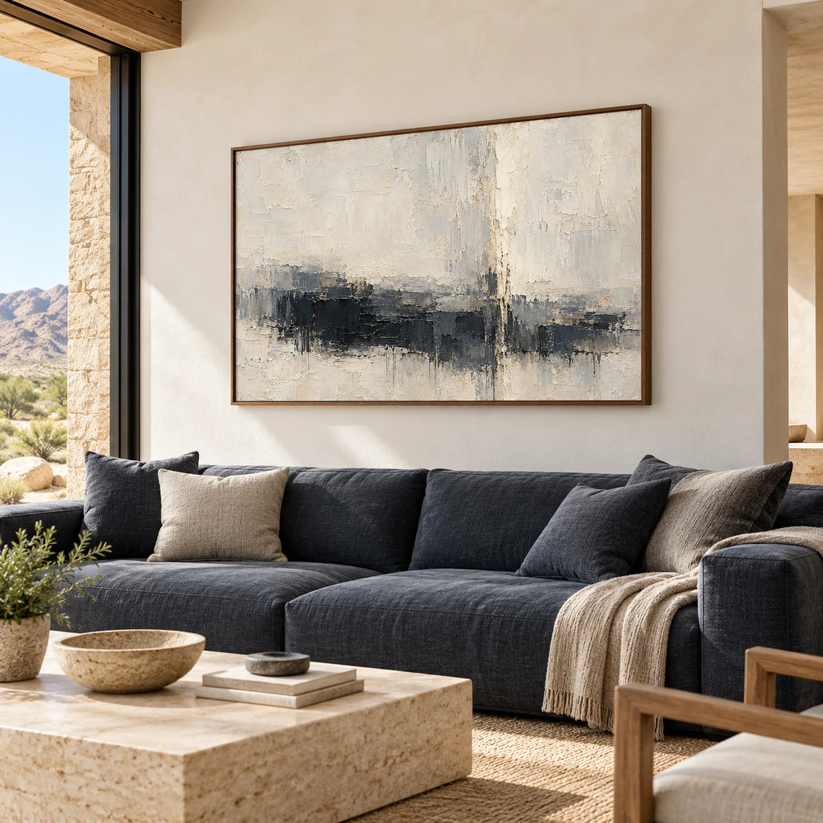 Charcoal and ivory abstract painting above a deep blue-gray sofa in a bright living room with light plaster walls and pale timber, viewed slightly from the left.