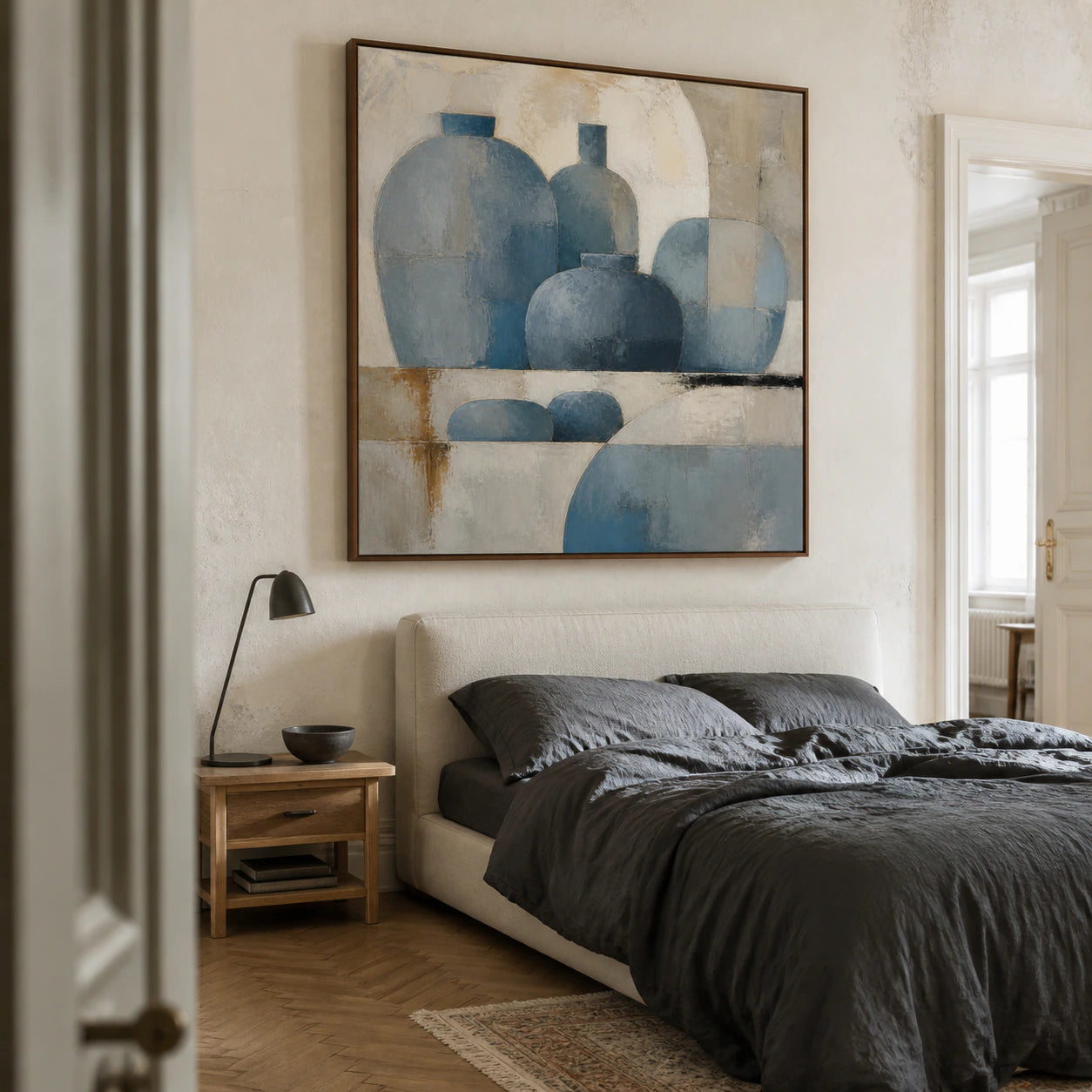 Square blue-grey geometric painting above a quiet bedroom furnishing.