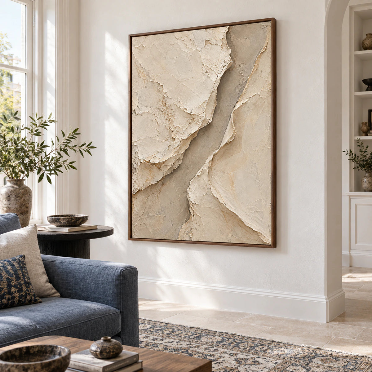 Vertical textured abstract painting above a restrained living-room seating arrangement in bright natural daylight.