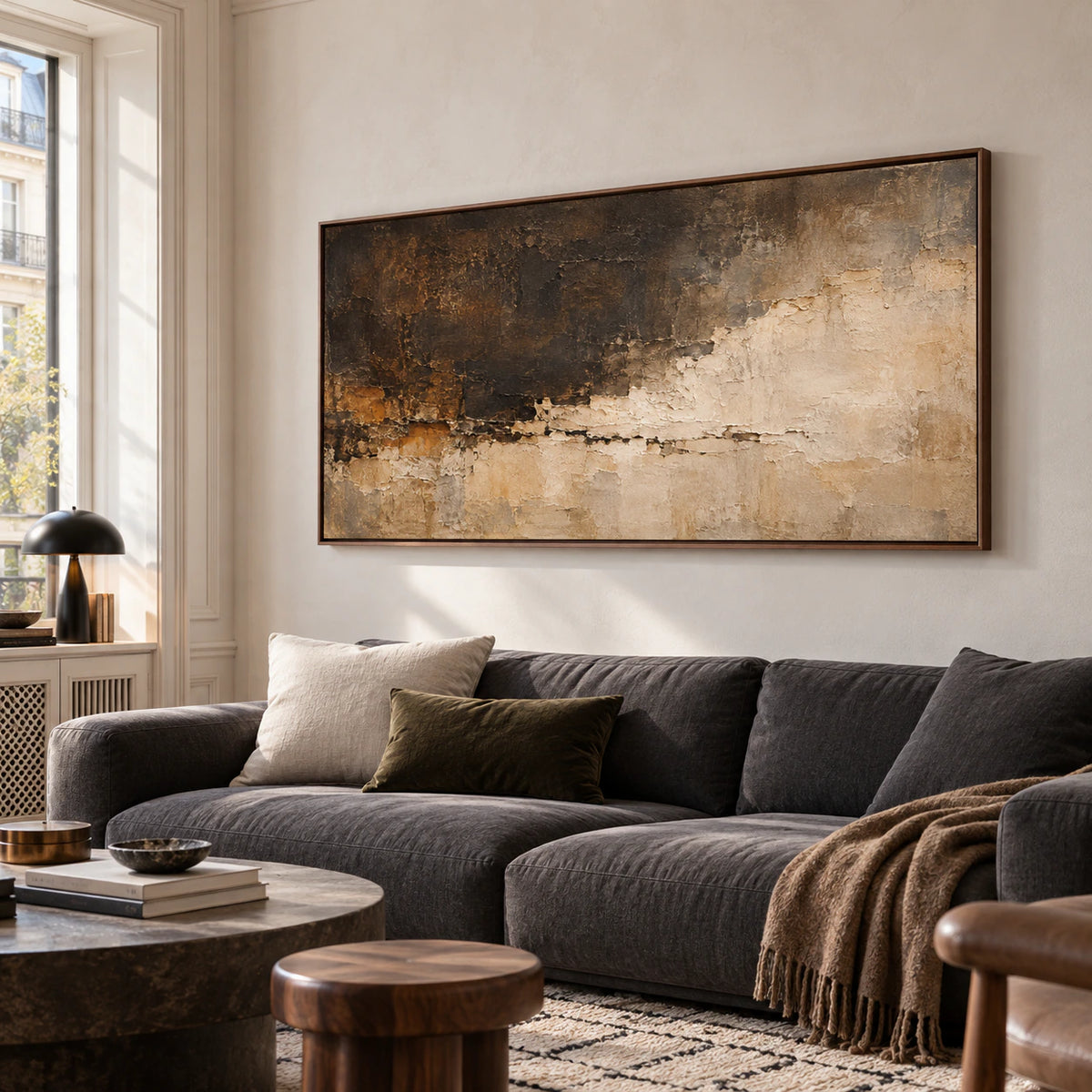 Fallow-Mantle above a charcoal sofa in a bright living room with pale plaster walls and black accents, viewed slightly from the left at seated eye level.
