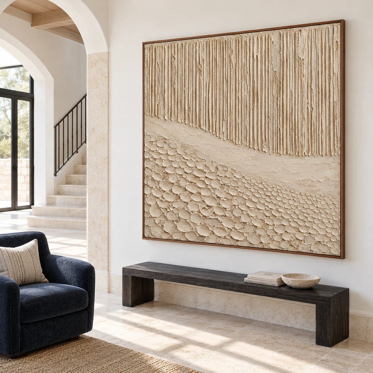 Square ivory and sand artwork on the main wall of a bright, spacious foyer with pale stone architecture and a dark narrow bench, viewed from the left.
