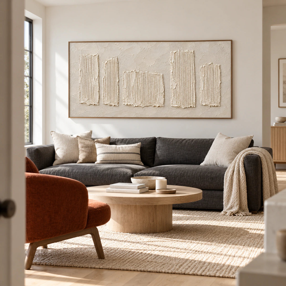 Large ivory ribbed relief artwork above a charcoal sofa in a bright, open living room.