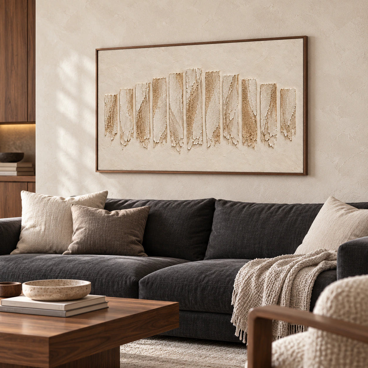 Ivory textured painting above a charcoal sofa against pale limestone, with a low walnut table in daylight, viewed from a slight left angle.