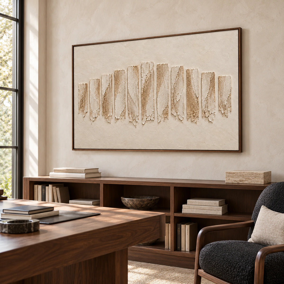 Ivory textured painting in a bright home office with a walnut desk, black reading chair and open shelving, viewed from the right at standing height.