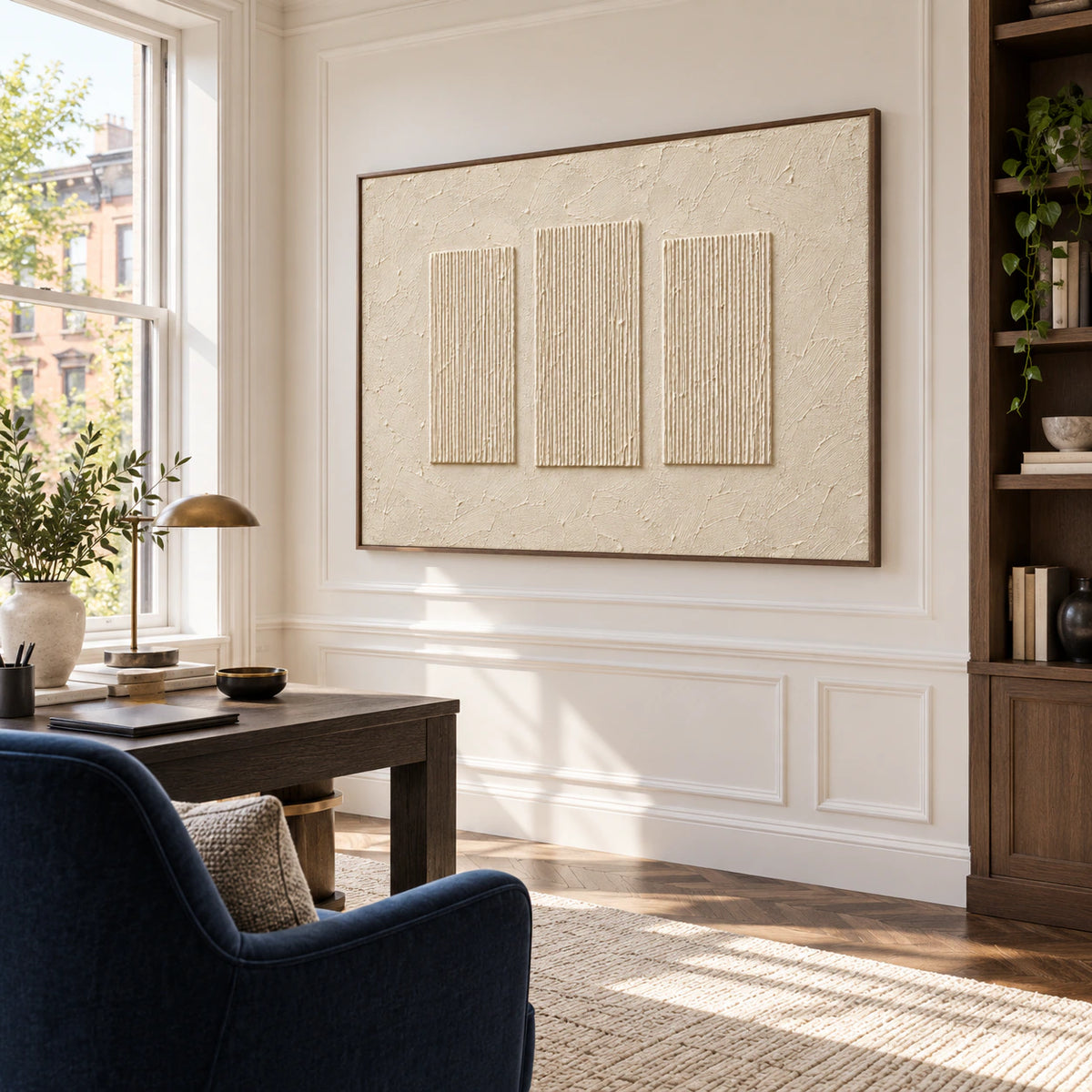 Ivory ribbed artwork on a white wall beside a dark desk and deep blue reading chair, viewed from the right in a bright home office.