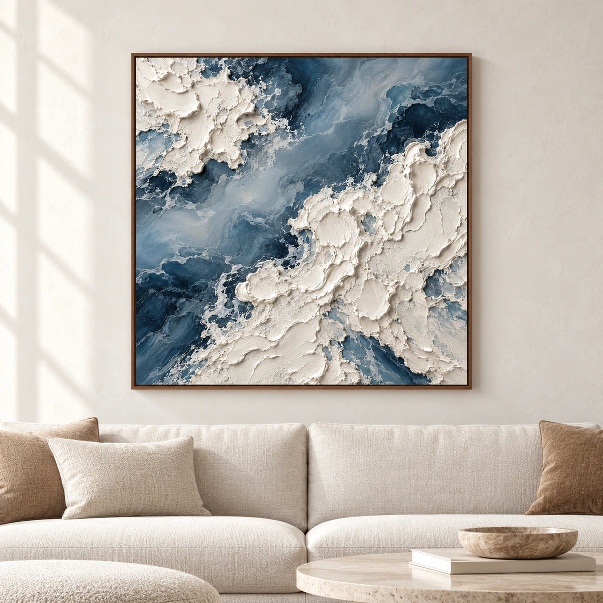 Square blue-and-ivory impasto painting displayed on the main wall of a bright living room with a sofa and restrained neutral furnishings, viewed straight-on.