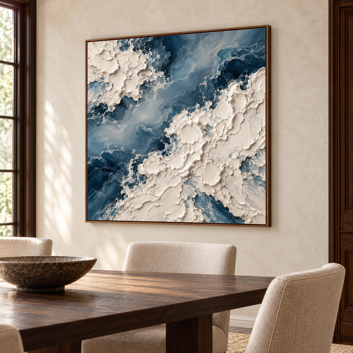 Square blue-and-ivory abstract painting on a softly textured pale dining room wall above a dark wood table and neutral chairs, viewed from the right.