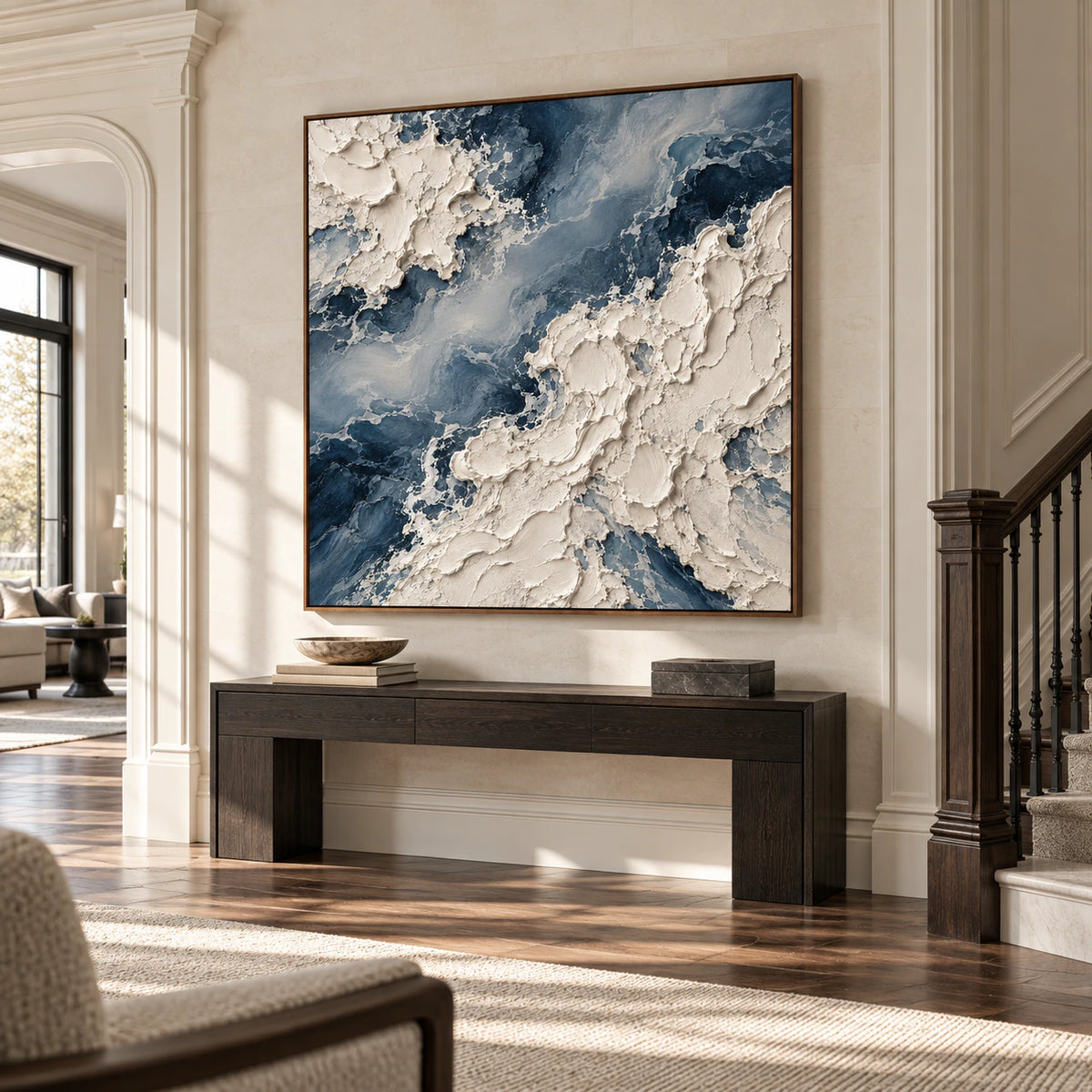 Square blue-and-ivory impasto painting centered on a pale limestone foyer wall with a dark console, viewed from a low left angle in bright daylight.