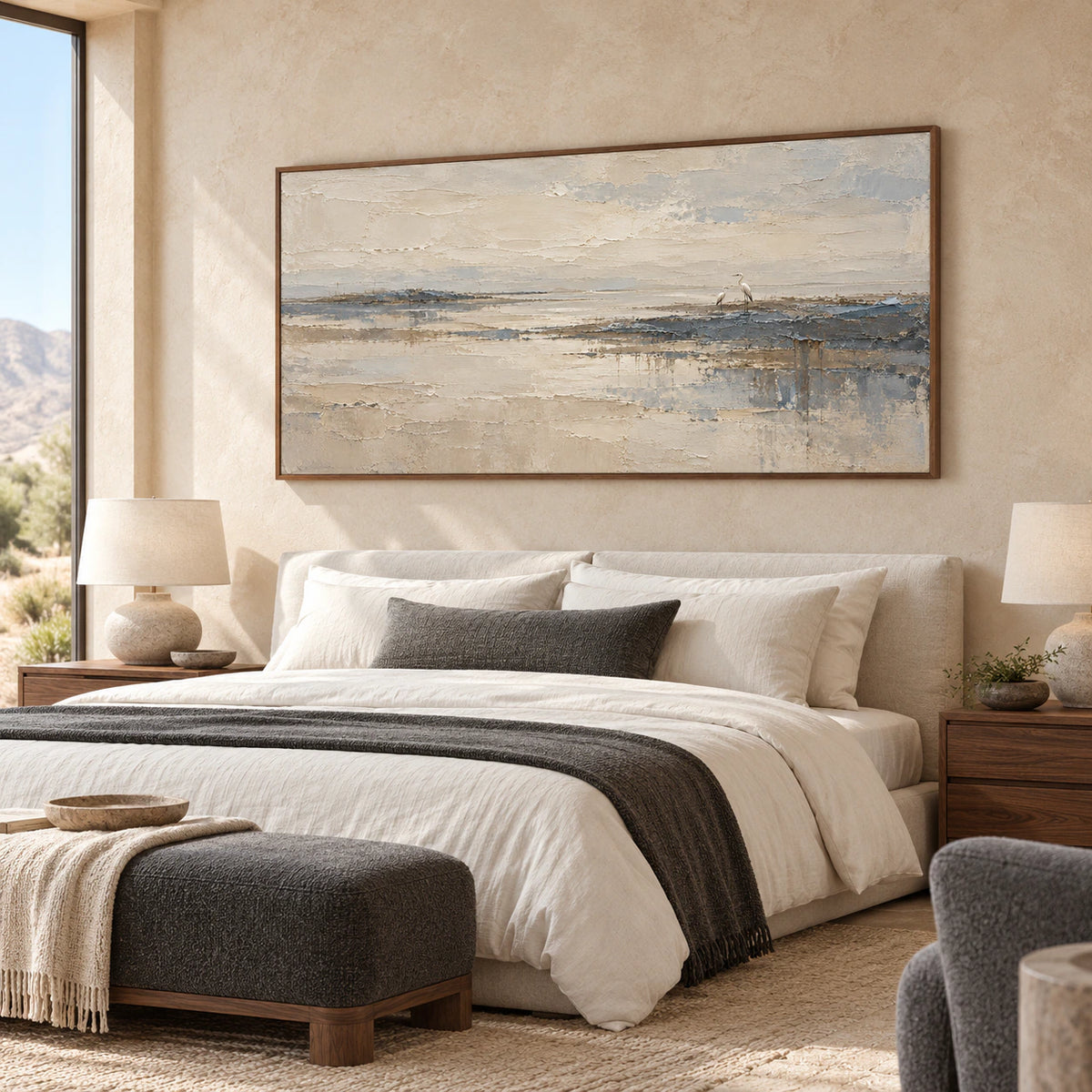 Wide shoreline painting above a low bed with white linen, walnut nightstands and a muted slate accent chair in a bright bedroom, viewed from a low right angle.