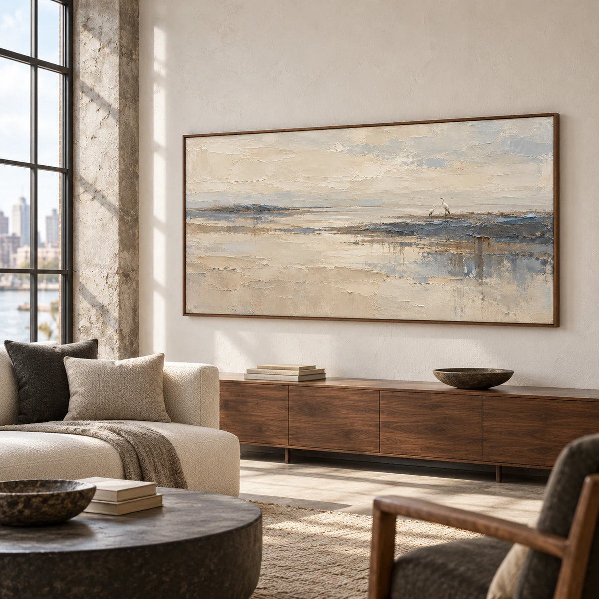 Heron shoreline painting in a bright hospitality loft with exposed concrete columns, charcoal and ivory lounge seating and tall industrial windows, viewed from the left.