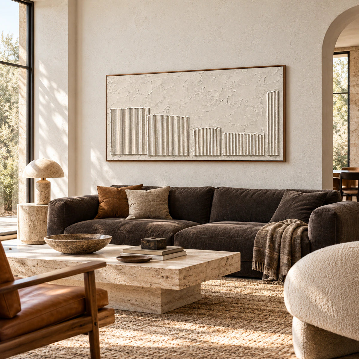 Ivory textured painting above a dark sofa in a bright, open living room with daylight entering through tall side windows.