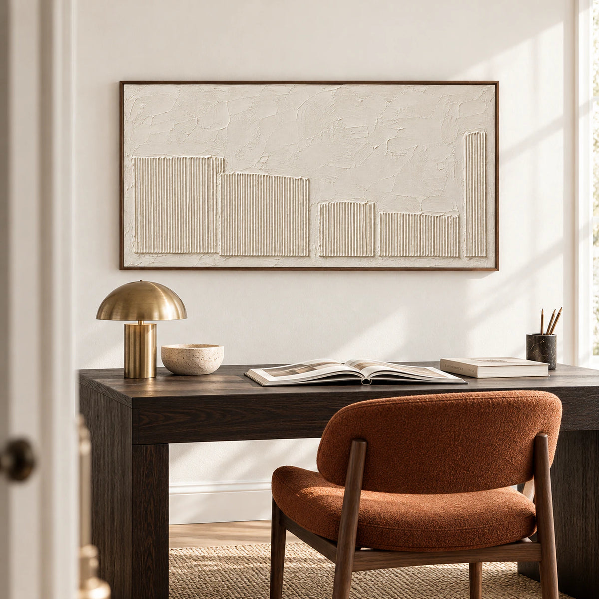 Ivory textured painting above a dark timber desk beside a simple reading chair in an airy home office, viewed from an elevated position.