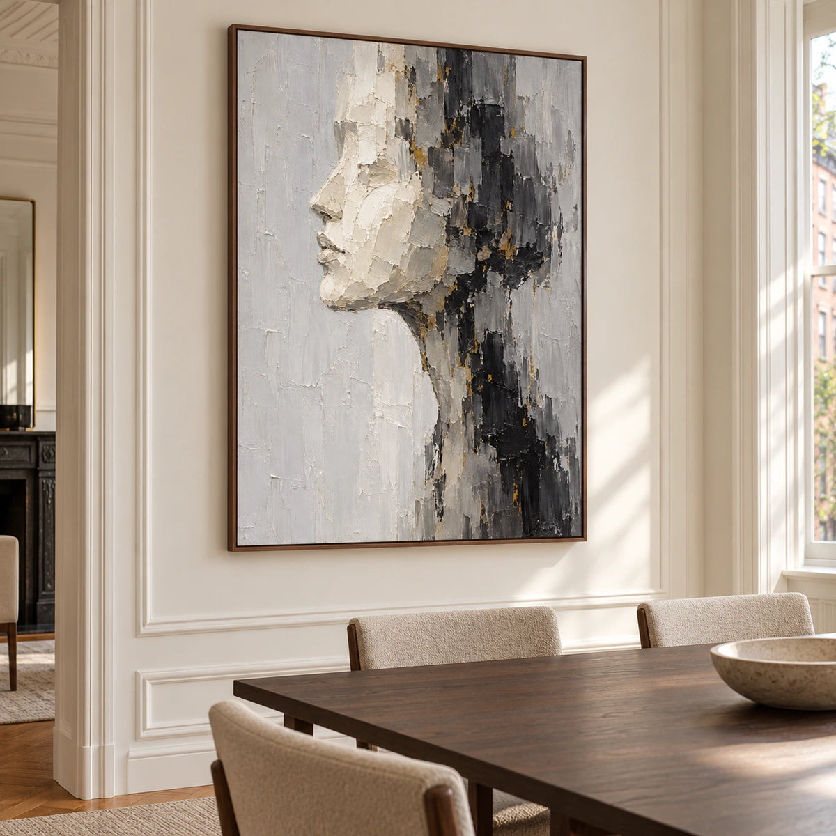 Vertical ivory profile painting on a warm white wall in a bright dining room with a dark timber table and simple chairs, viewed from the right with daylight entering from the right.