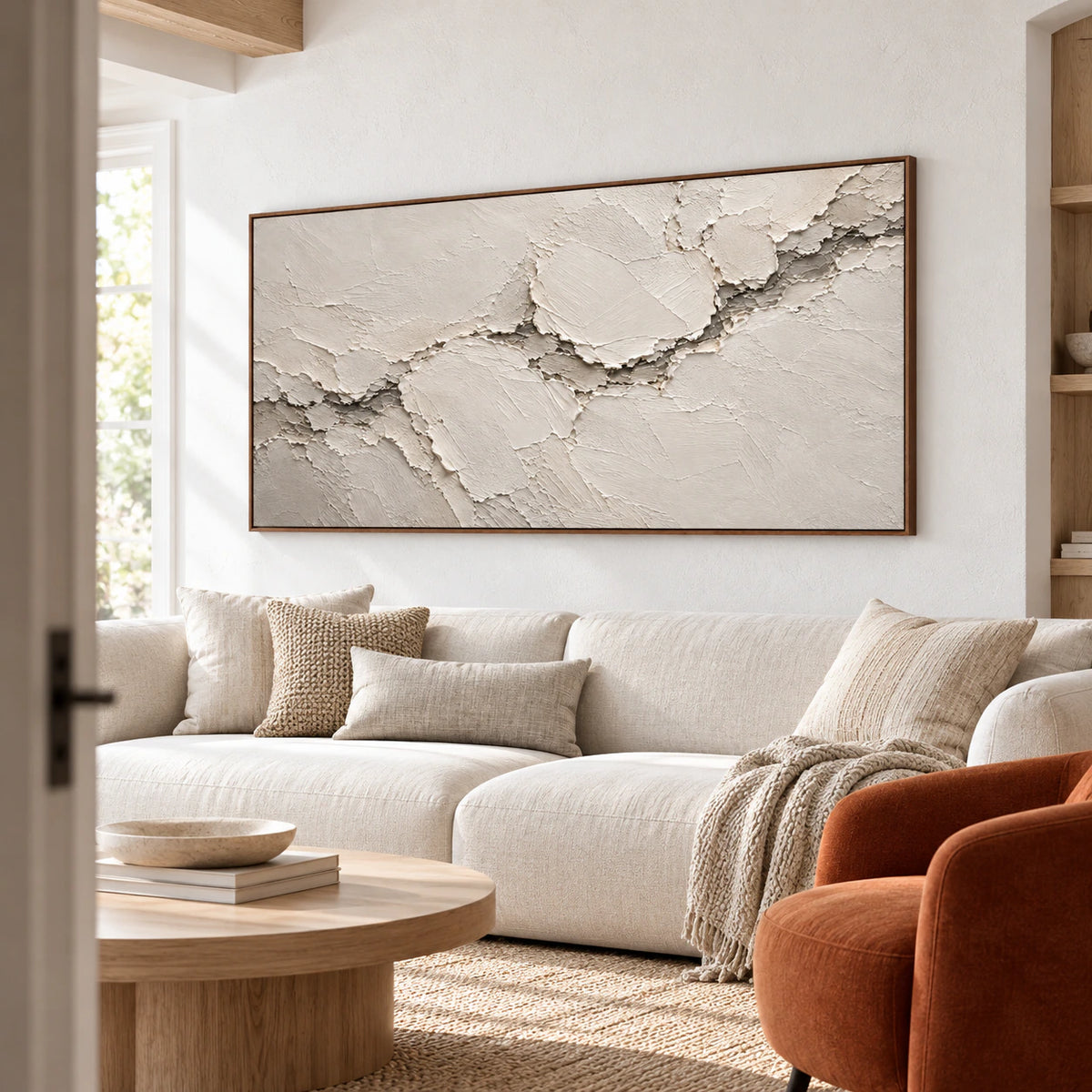 Ivory and cream relief artwork above a restrained sofa in a bright living room.