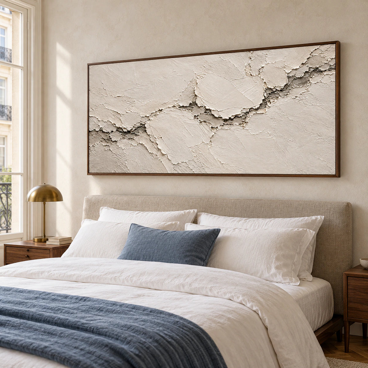 Ivory relief artwork above a simply furnished bed in a quiet, sunlit bedroom.