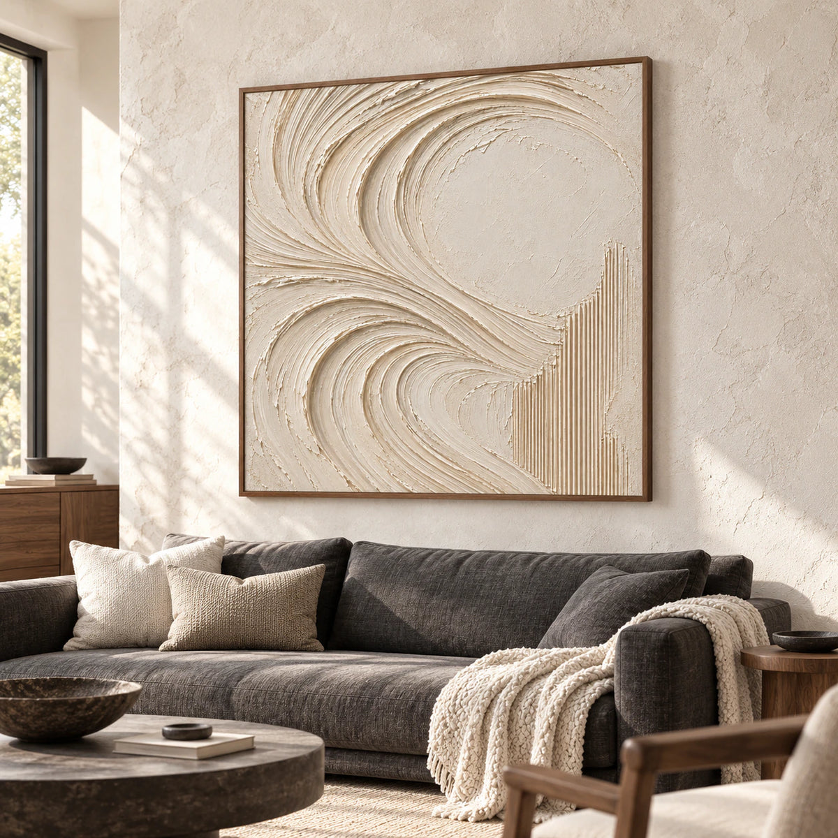Large square ivory abstract painting above a charcoal sofa, viewed from a slight left angle in a bright living room with a pale stone wall and walnut side table.