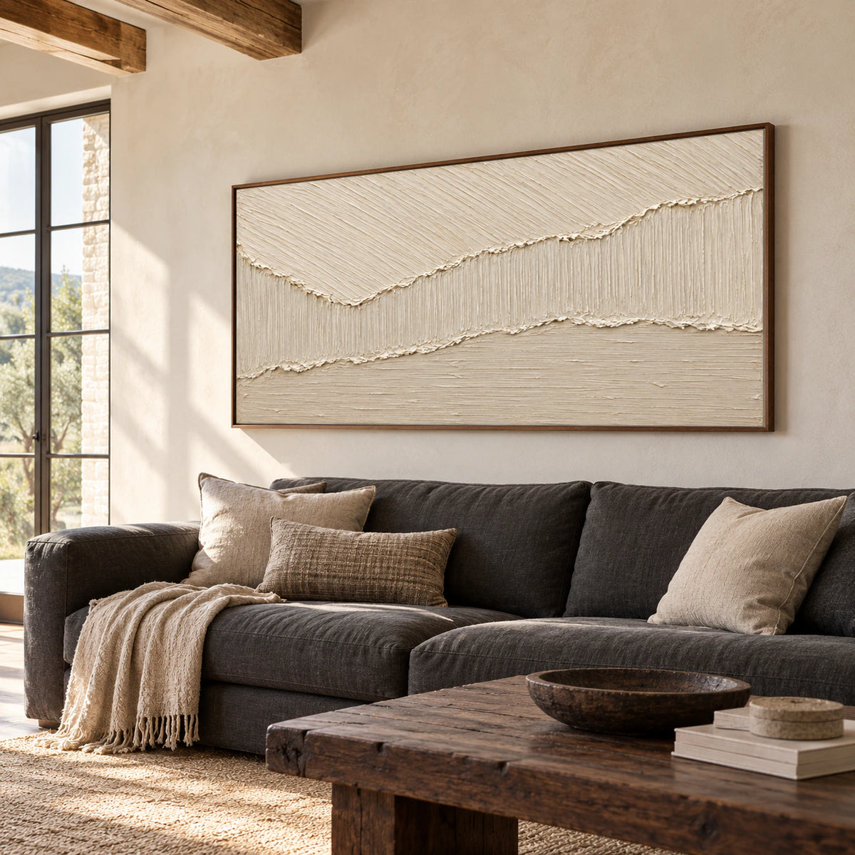 Ivory and beige textured abstract painting displayed above a charcoal sofa in a bright living room with broad windows.
