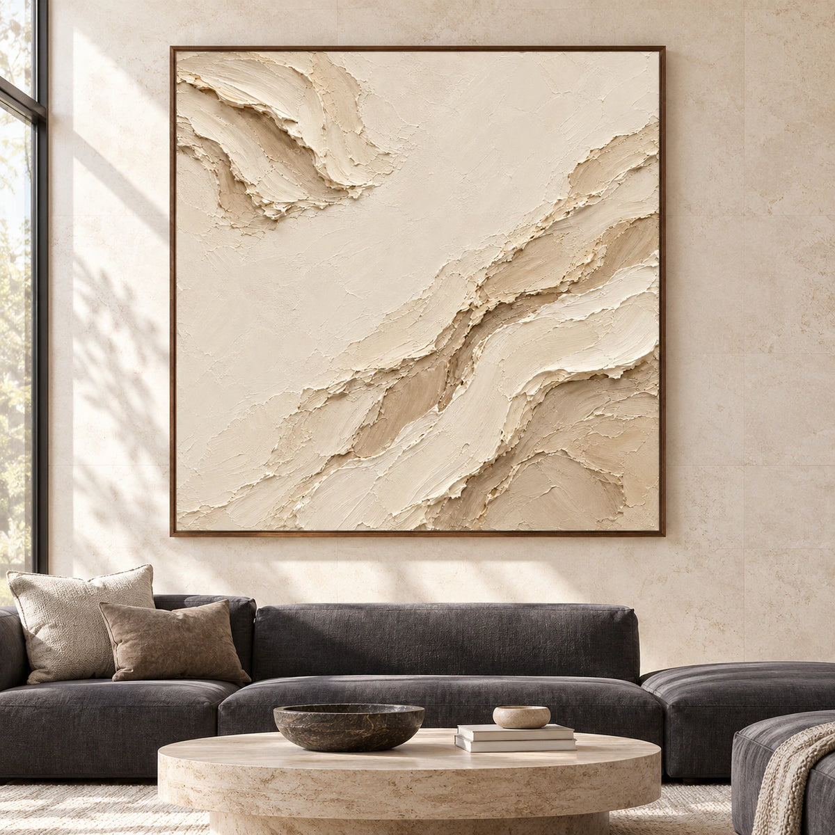 Large square ivory and sand abstract painting on a pale limestone wall above low charcoal seating in a bright living room, viewed straight on.