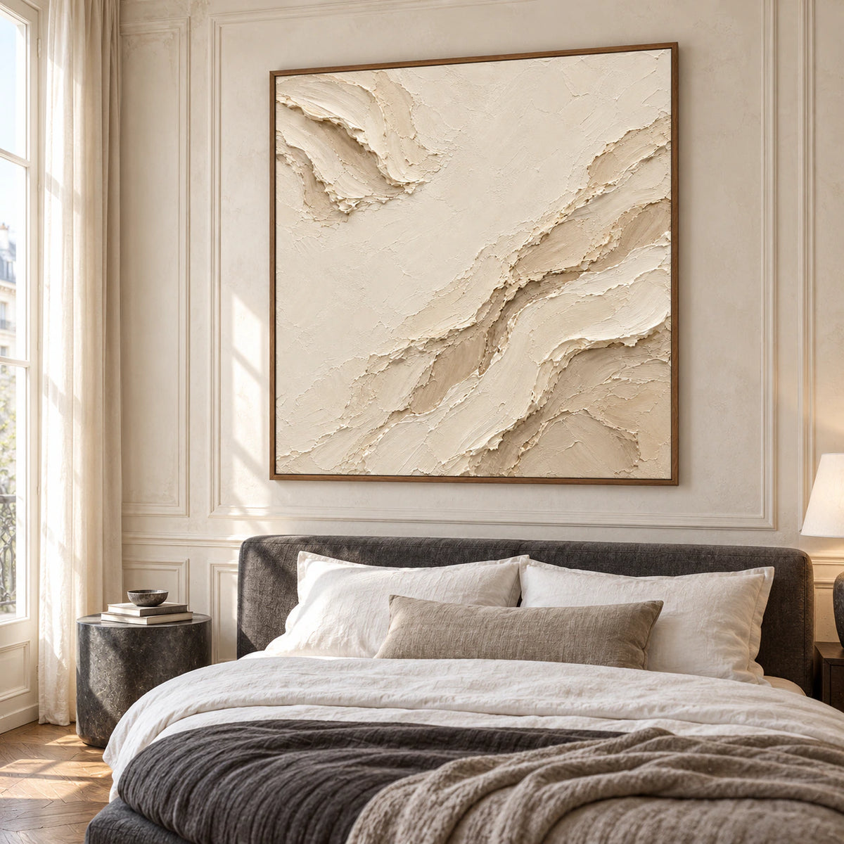 Square ivory and sand abstract painting above a low charcoal upholstered bed with white linen, a slate bedside table and wall paneling, viewed from the left.