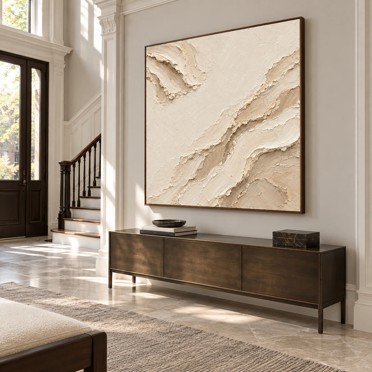 Large square ivory and sand abstract painting on a pale grey foyer wall, with stone flooring, a dark bronze console and clerestory windows, viewed from low left.