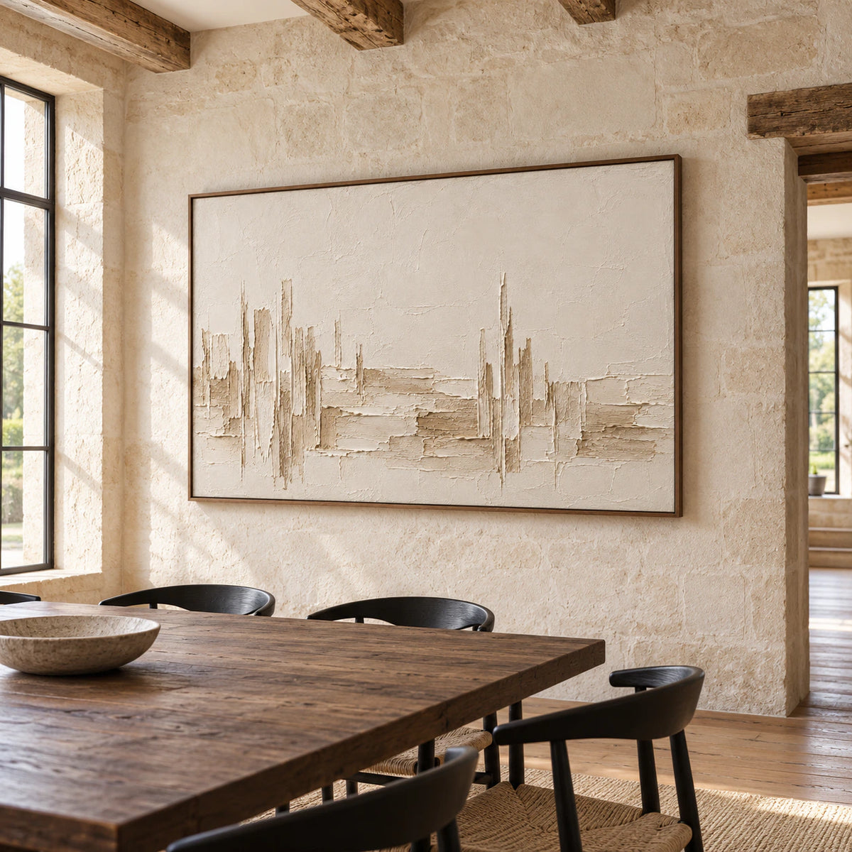 Ivory textured painting on a light limestone wall above a dark oak dining table with black chairs, viewed slightly from the right in daylight.