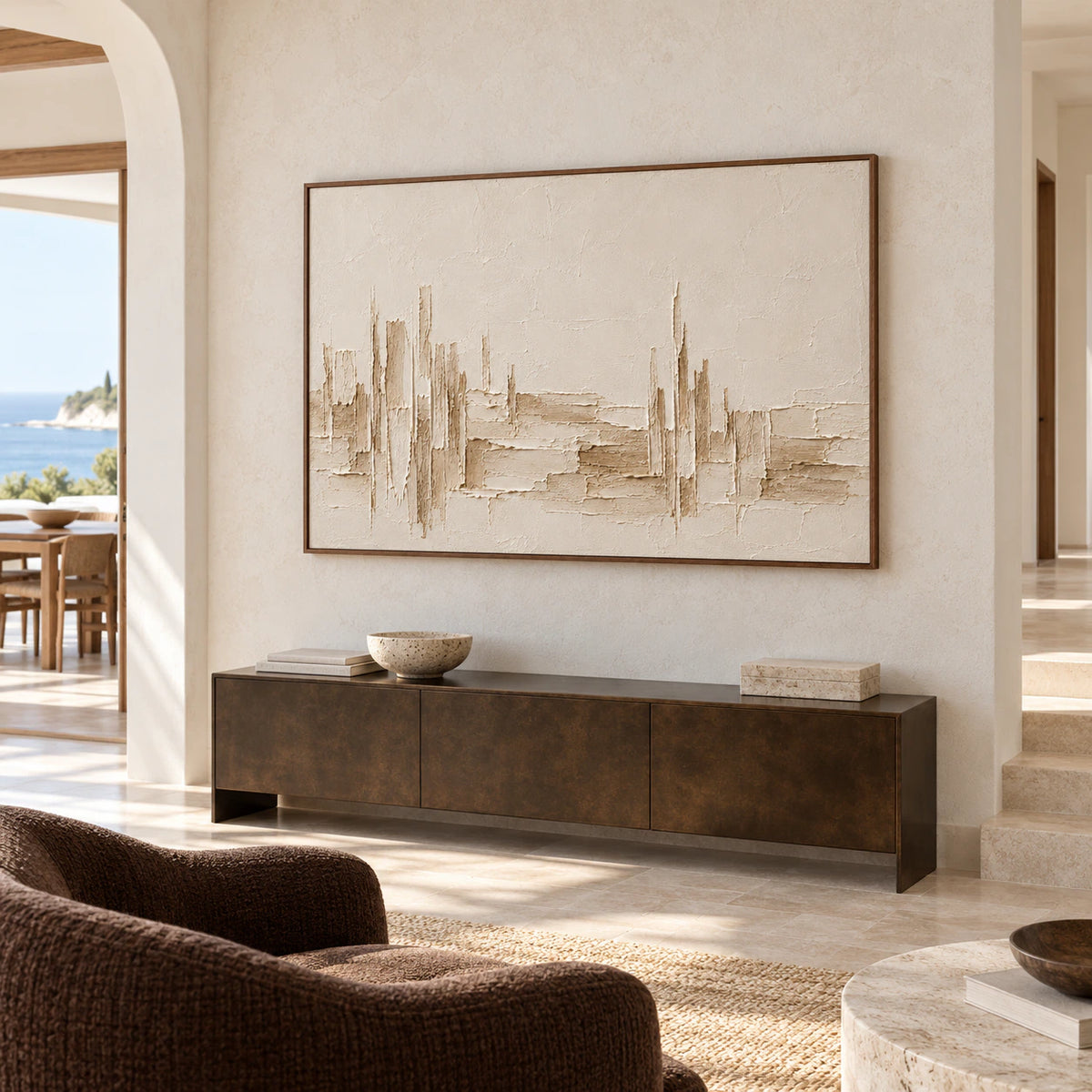 Large ivory and sand textured painting above a dark bronze console on a tall pale stone foyer wall, viewed from a left-side approach in daylight.