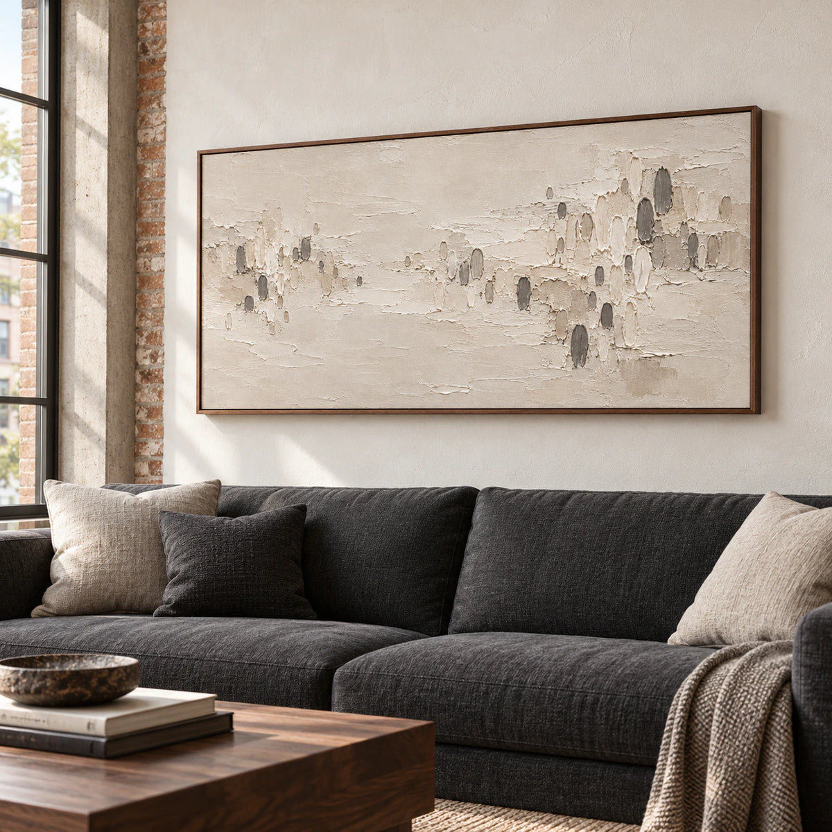 Large horizontal ivory and charcoal textured abstract painting above a restrained charcoal sofa in a bright living room.