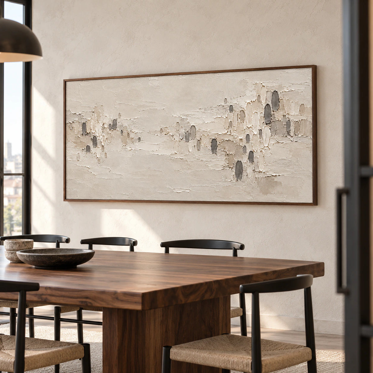 Prominent ivory and sand abstract painting with scattered dark marks on a pale dining room wall above a long walnut table.