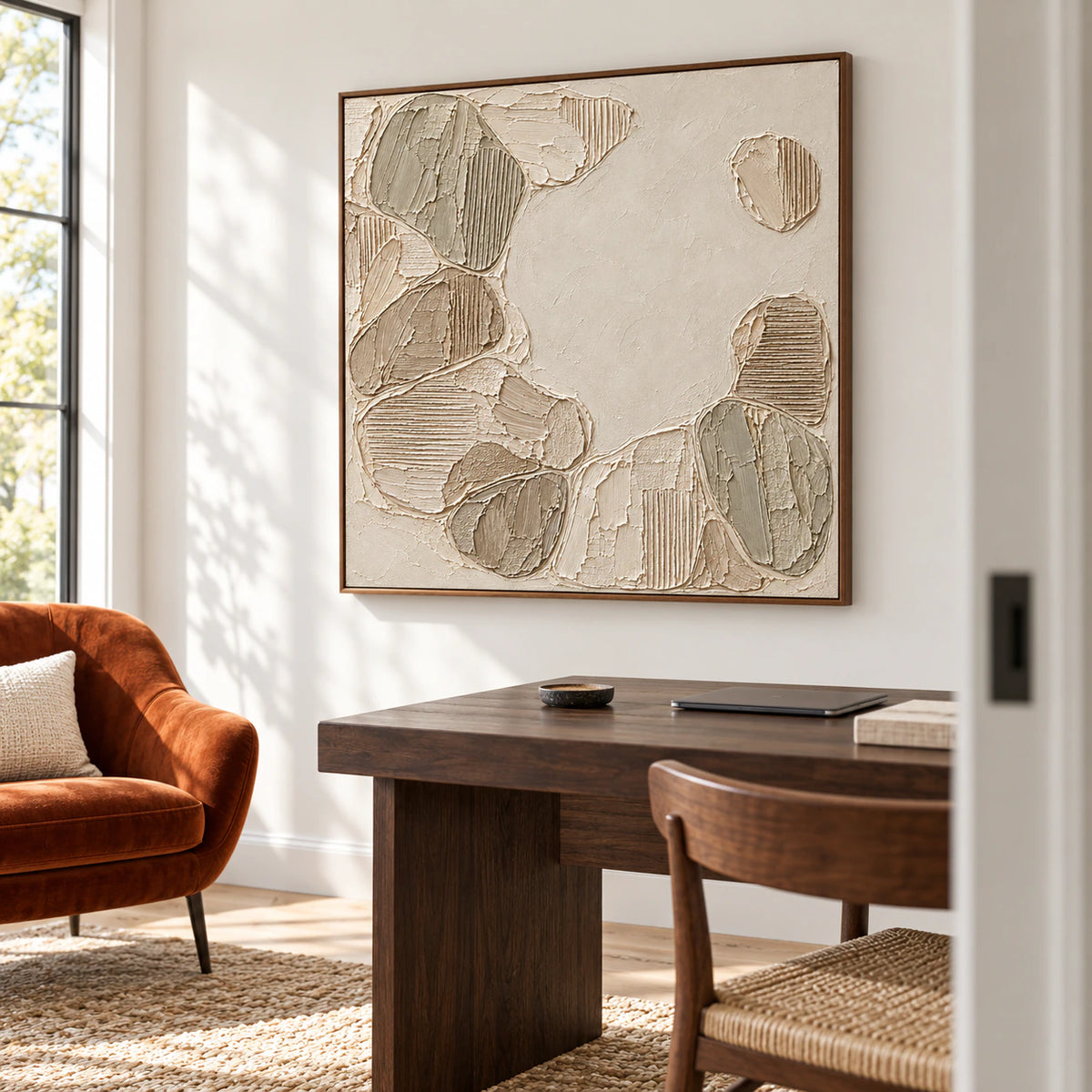 Square ivory and taupe textured painting on a pale wall beside a dark timber desk and simple chair, viewed from the right in a bright home office.