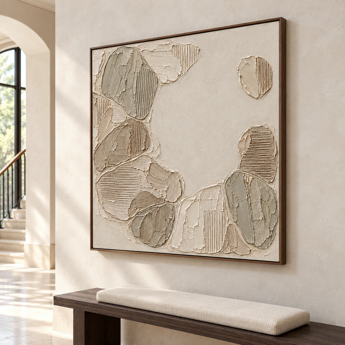 Large square ivory and taupe textured painting on a tall limestone wall in a bright foyer, viewed from a low left angle with stone flooring and a dark bench.