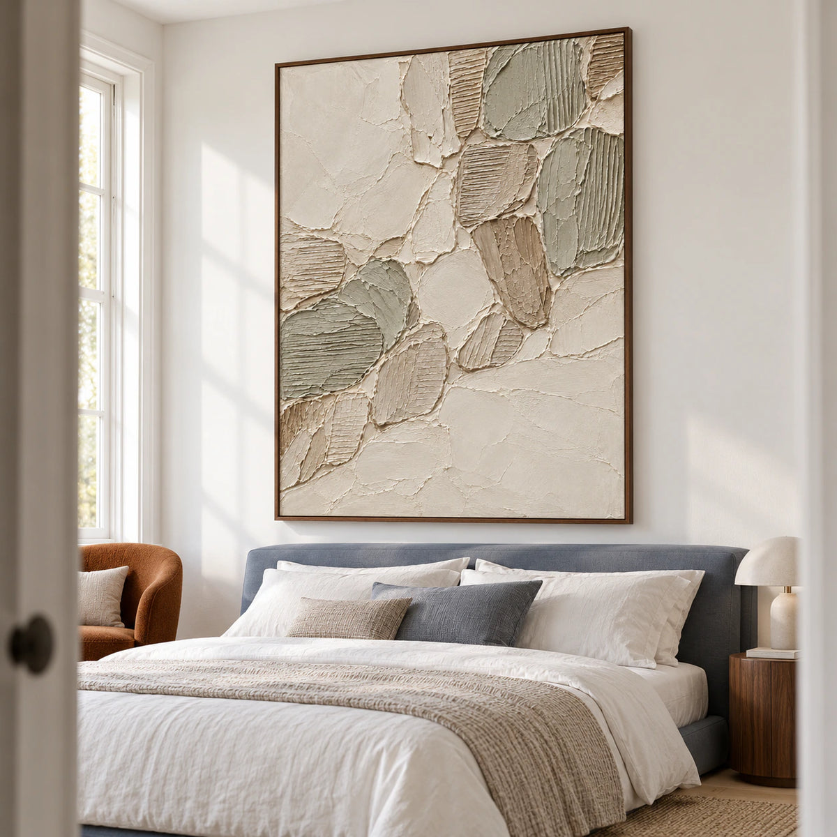 Vertical Linen-Tesserae artwork above a low slate-blue bed with white bedding, viewed from the left slightly below eye level in a bright bedroom.