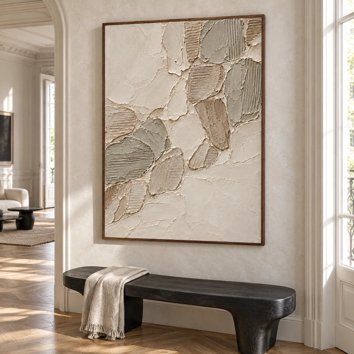 Large vertical Linen-Tesserae artwork on a cool limestone wall above a sculptural black bench in a bright foyer with wood flooring, viewed from the left at a slightly elevated angle.