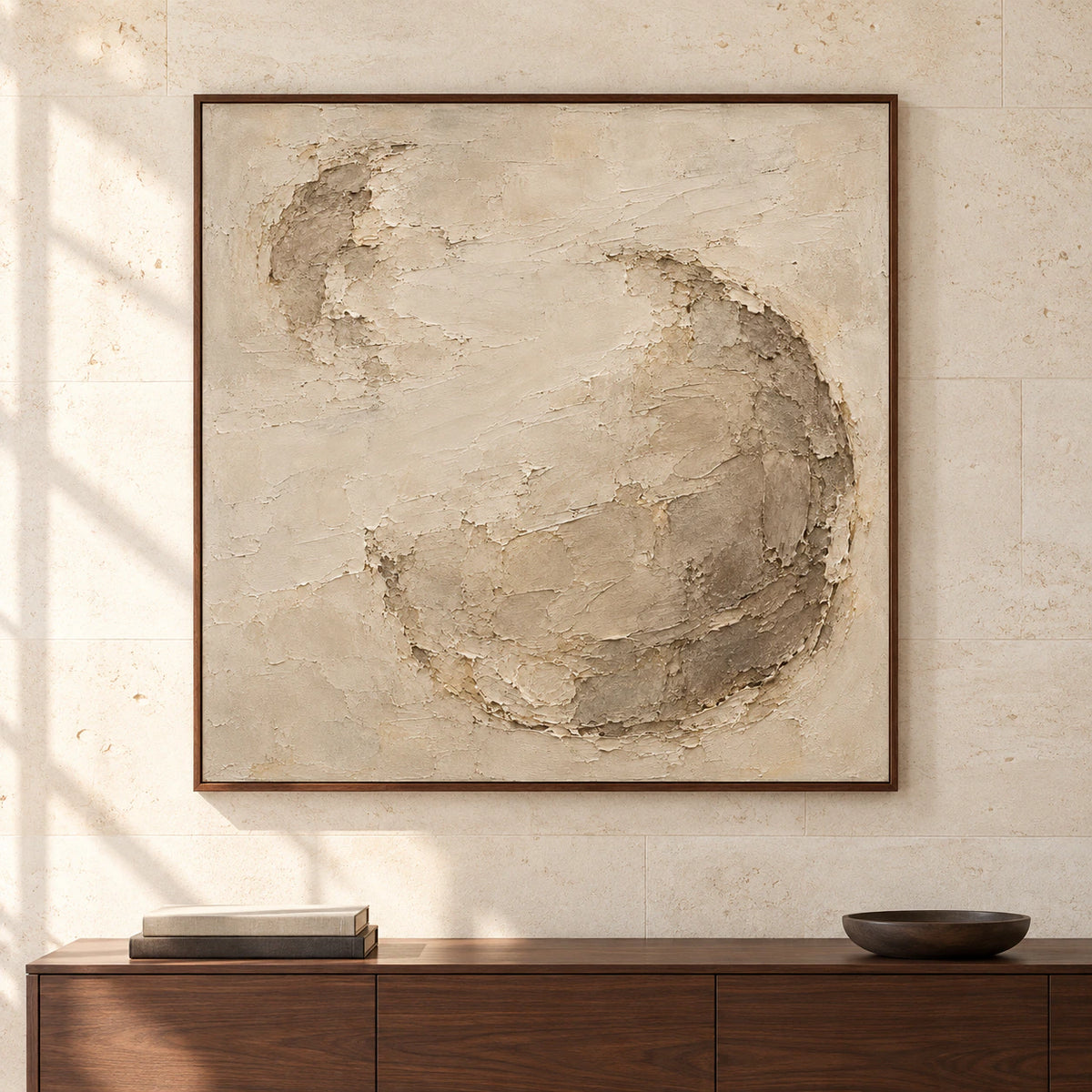 Large square abstract artwork with a rounded taupe relief against warm ivory displayed on a wall in a spacious room.