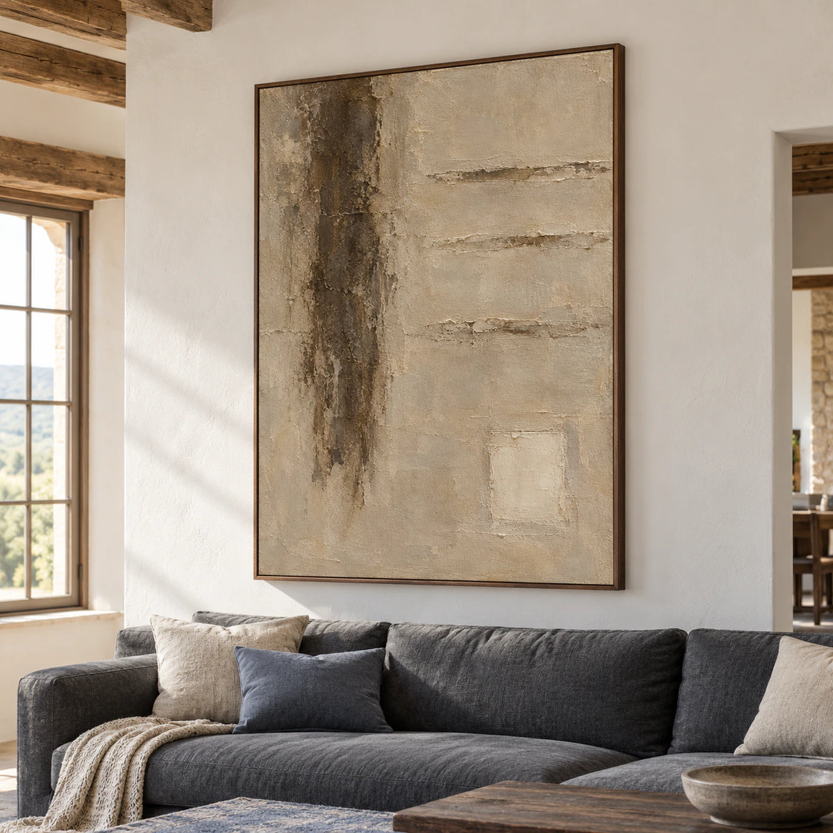 Vertical textured abstract painting above a low charcoal sofa, viewed from the left in a bright living room with a blue-grey rug and dark wood accents.