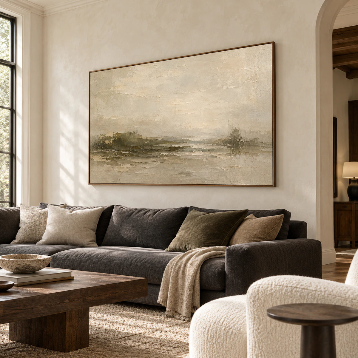 Large horizontal painting above a charcoal sofa on a pale neutral wall in a bright living room, viewed from the left at standing eye level.