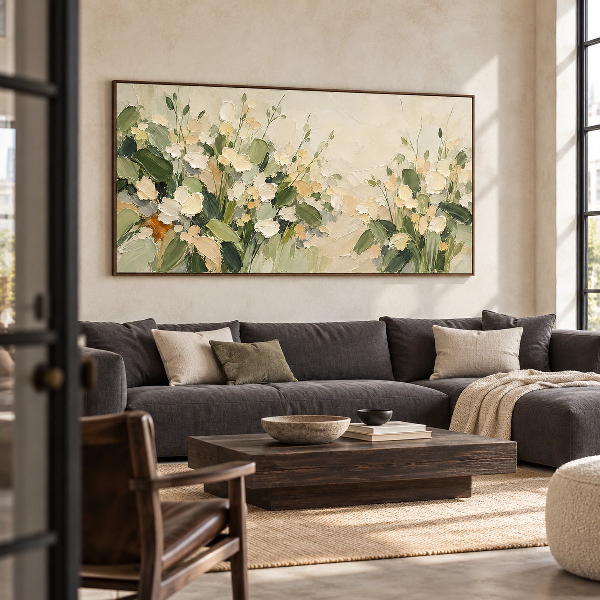 Large floral painting above a charcoal linen sofa in a bright living room with pale plaster walls, viewed from a slight left angle.