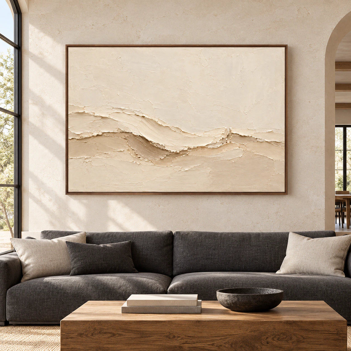 Large warm ivory abstract painting viewed straight-on on a pale stone wall in an open living space with charcoal and natural wood furnishings.