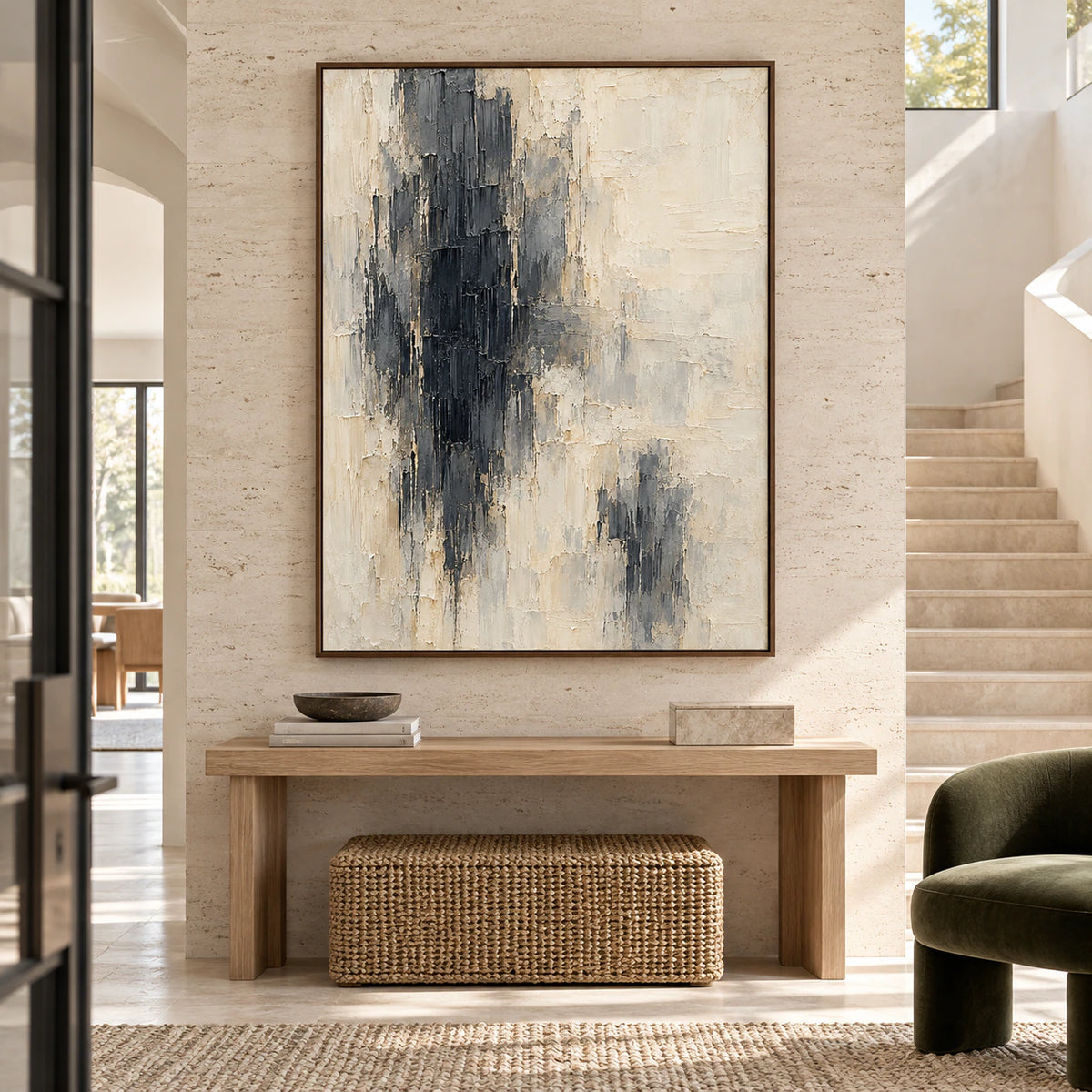 Obsidian-Pillars on a pale travertine wall beside a sculptural staircase and narrow console in a tall foyer, viewed from an elevated left angle.