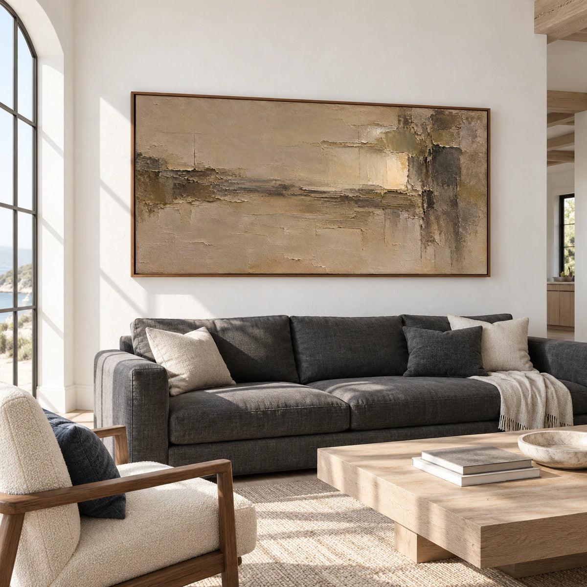 Ochre and umber abstract painting above a charcoal sofa in a bright living room with pale walls, viewed from a left-oblique angle.