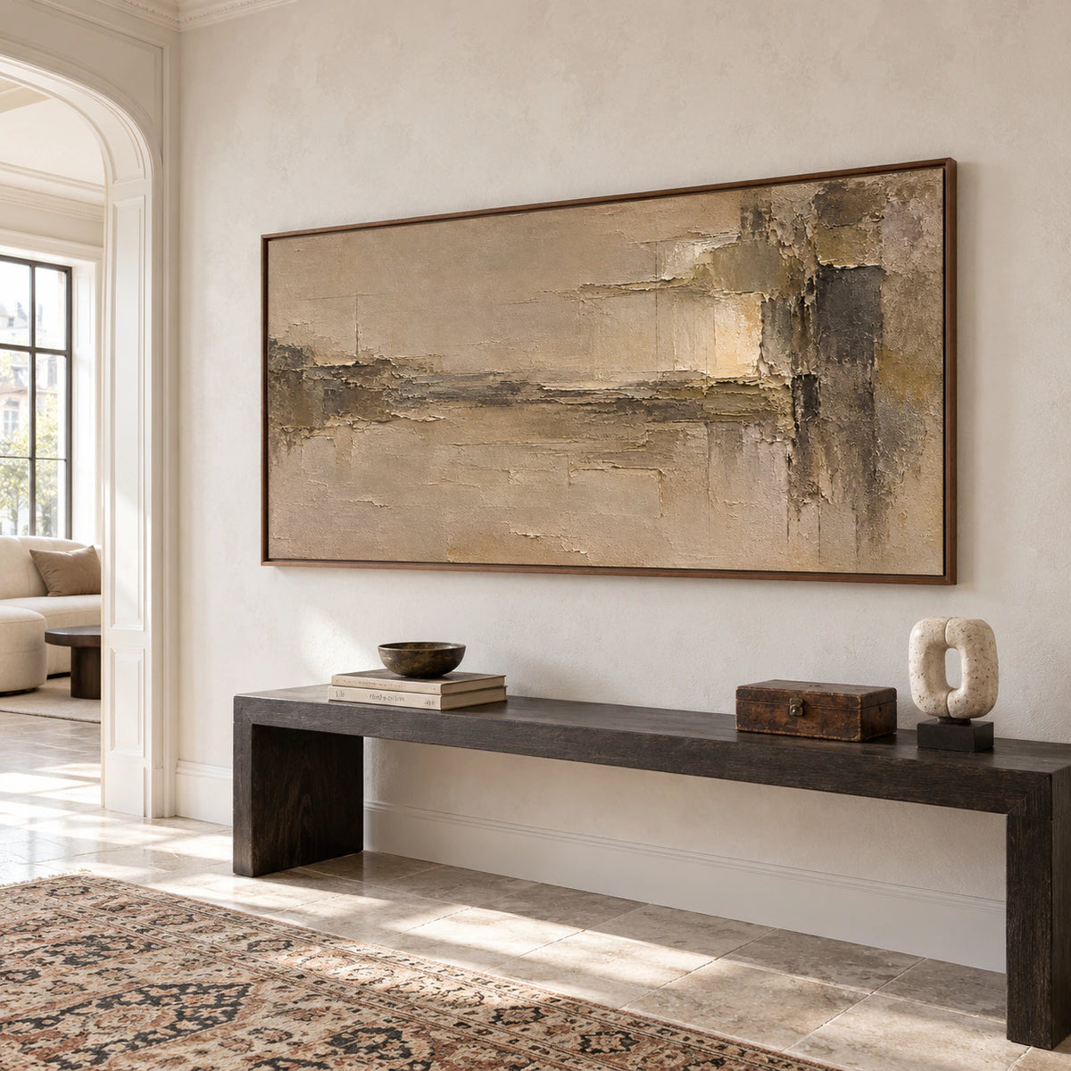 Large ochre and umber painting on a pale plaster wall above a dark console in a bright foyer with a high ceiling and stone floor, viewed from the left.