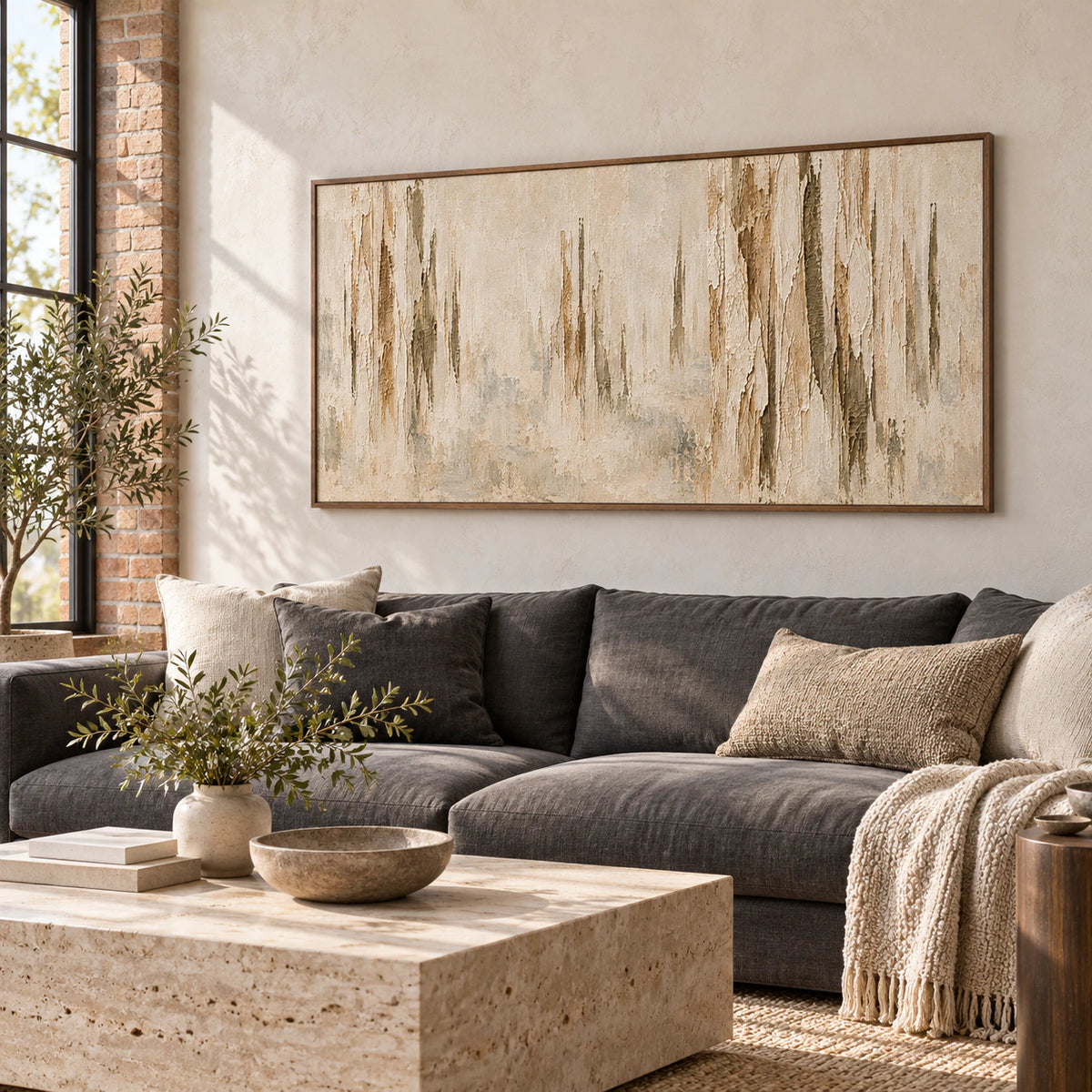 Large wide abstract painting displayed above a restrained charcoal sofa in a bright living room with pale plaster walls and natural daylight.