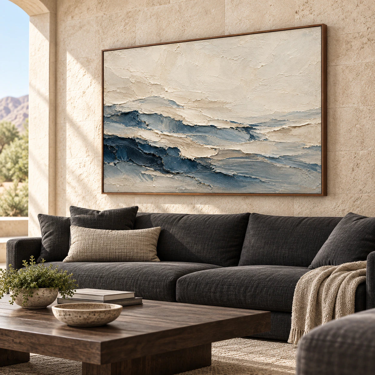 Cream and slate blue abstract painting above a warm-gray sofa, viewed from the left in a bright living room with a dark timber table.